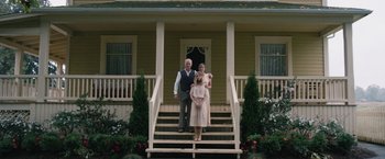 Movie still from “1922” (2017), directed by Zak Hilditch – A man , woman and a baby standing on the front steps of a house; Wide shot, Low angle