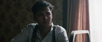 Movie still from “1922” (2017), directed by Zak Hilditch – A young man in a striped shirt and suspenders looks to his left; Close Up shot, Over the shoulder angle