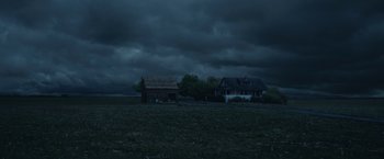 Movie still from “1922” (2017), directed by Zak Hilditch – A house and a barn in the middle of a field under a cloudy sky; Extreme Wide shot, Low angle
