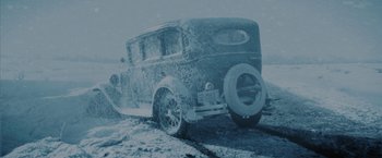 Movie still from “1922” (2017), directed by Zak Hilditch – An old car is covered in snow on the road; Wide shot, High angle