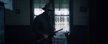 Movie still from “1922” (2017), directed by Zak Hilditch – A man holding a baseball bat in front of a table; Medium shot, Low angle
