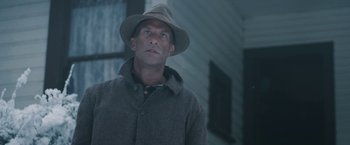 Movie still from “1922” (2017), directed by Zak Hilditch – A man wearing a hat standing in front of a building; Close Up shot, Low angle