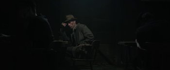 Movie still from “1922” (2017), directed by Zak Hilditch – A man sitting at a table in a dark room; Medium shot, Over the shoulder angle