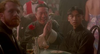 Movie still from “Shanghai Triad” (1995), directed by Yimou Zhang – A man sitting at a table with a rose in front of him; Medium shot, Over the shoulder angle