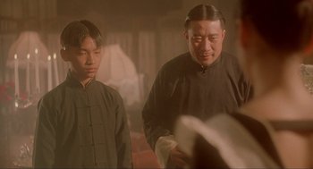 Movie still from “Shanghai Triad” (1995), directed by Yimou Zhang – A man and a young boy standing next to each other; Medium shot, Over the shoulder angle
