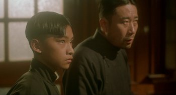 Movie still from “Shanghai Triad” (1995), directed by Yimou Zhang – A man standing next to a young boy in front of a wall; Close Up shot, Over the shoulder angle