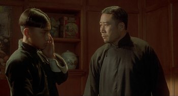 Movie still from “Shanghai Triad” (1995), directed by Yimou Zhang – A man and a woman standing next to each other in a room; Medium shot, Over the shoulder angle