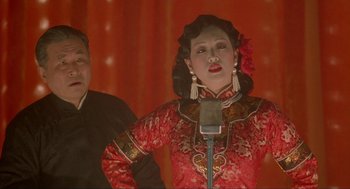 Movie still from “Shanghai Triad” (1995), directed by Yimou Zhang – A woman in a red and black dress is singing; Medium shot, Over the shoulder angle