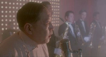 Movie still from “Shanghai Triad” (1995), directed by Yimou Zhang – A man is singing into a microphone in front of a group of people; Close Up shot, Low angle