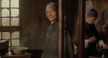 Movie still from “Shanghai Triad” (1995), directed by Yimou Zhang – An older man standing next to a wooden pole; Medium shot, Over the shoulder angle