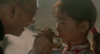 Movie still from “Shanghai Triad” (1995), directed by Yimou Zhang – An older person feeding a young girl with chopsticks; Close Up shot, Over the shoulder angle