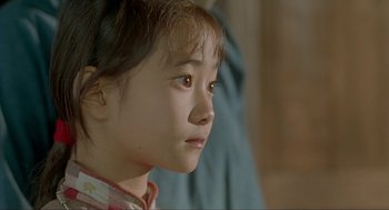 Movie still from “Shanghai Triad” (1995), directed by Yimou Zhang – A little girl looking to her left with a serious look; Close Up shot, Over the shoulder angle