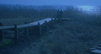 Movie still from “Shanghai Triad” (1995), directed by Yimou Zhang – Two people sitting on a wooden bridge in a field; Extreme Wide shot, High angle