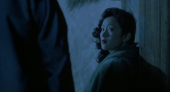 Movie still from “Shanghai Triad” (1995), directed by Yimou Zhang – A young woman with blue eyes is standing in the dark; Close Up shot, Over the shoulder angle