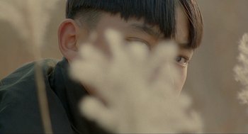 Movie still from “Shanghai Triad” (1995), directed by Yimou Zhang – A young man with short black hair is looking at the camera; Extreme Close Up shot, Over the shoulder angle