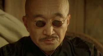 Movie still from “Shanghai Triad” (1995), directed by Yimou Zhang – An older man with a bald head wearing sunglasses; Close Up shot, Low angle