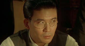 Movie still from “Shanghai Triad” (1995), directed by Yimou Zhang – A person wearing a suit and glasses; Close Up shot, Over the shoulder angle