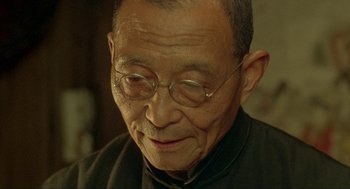 Movie still from “Shanghai Triad” (1995), directed by Yimou Zhang – An older man wearing glasses and a black shirt; Close Up shot, Over the shoulder angle