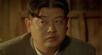 Movie still from “Shanghai Triad” (1995), directed by Yimou Zhang – A person wearing a suit and tie; Close Up shot, Over the shoulder angle