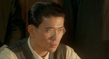 Movie still from “Shanghai Triad” (1995), directed by Yimou Zhang – A person wearing a suit and glasses; Close Up shot, Over the shoulder angle