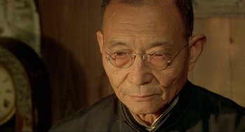 Movie still from “Shanghai Triad” (1995), directed by Yimou Zhang – An older man wearing glasses and a black shirt; Close Up shot, Over the shoulder angle