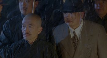 Movie still from “Shanghai Triad” (1995), directed by Yimou Zhang – A man in a suit and hat standing next to another man in a suit; Close Up shot, Over the shoulder angle