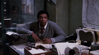 Movie still from “Sharky's Machine” (1981), directed by Burt Reynolds – A man sitting at a desk in front of papers; Medium shot, Low angle