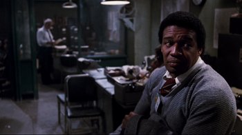 Movie still from “Sharky's Machine” (1981), directed by Burt Reynolds – A man sitting at a table in a room; Medium shot, Over the shoulder angle