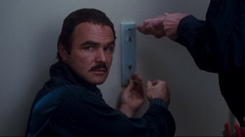 Movie still from “Sharky's Machine” (1981), directed by Burt Reynolds – A man with a mustache is holding a screwdriver in front of a wall; Close Up shot, Low angle