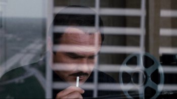 Movie still from “Sharky's Machine” (1981), directed by Burt Reynolds – A man with a mustache is holding a cigarette in front of a window; Close Up shot, Low angle