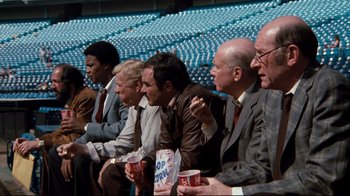 Movie still from “Sharky's Machine” (1981), directed by Burt Reynolds – A group of men sitting next to each other in a stadium; Wide shot, High angle