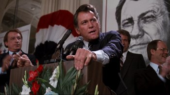 Movie still from “Sharky's Machine” (1981), directed by Burt Reynolds – A man is speaking at a podium with a microphone; Medium shot, Low angle