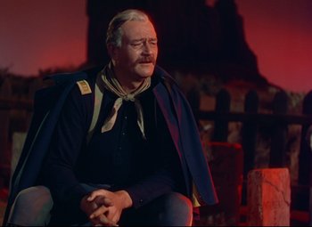 Movie still from “She Wore a Yellow Ribbon” (1949), directed by John Ford – An older man sitting on a chair in front of a red background; Medium shot, Over the shoulder angle