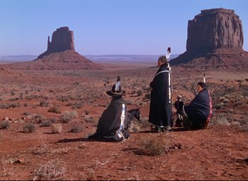 Movie still from “She Wore a Yellow Ribbon” (1949), directed by John Ford – A group of native americans sitting on the ground in the desert; Extreme Wide shot, Over the shoulder angle