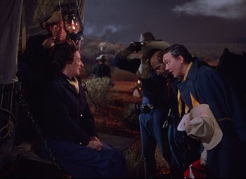 Movie still from “She Wore a Yellow Ribbon” (1949), directed by John Ford – A group of men standing around a woman in the dark; Medium shot, Over the shoulder angle