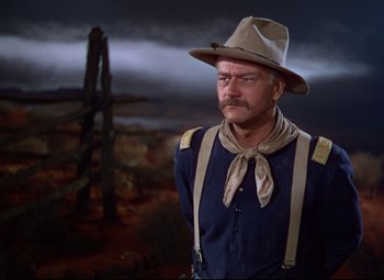 Movie still from “She Wore a Yellow Ribbon” (1949), directed by John Ford – A man wearing a hat and suspenders standing in front of a wooden structure; Medium shot, Low angle