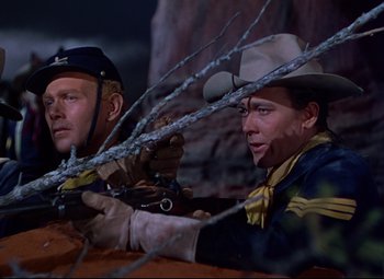 Movie still from “She Wore a Yellow Ribbon” (1949), directed by John Ford – A couple of men sitting next to each other holding guns; Medium shot, Low angle
