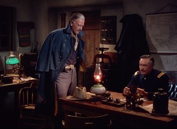 Movie still from “She Wore a Yellow Ribbon” (1949), directed by John Ford – A man standing next to a man sitting at a table; Medium shot, Over the shoulder angle