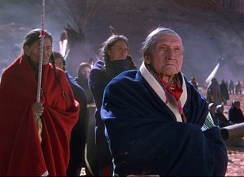 Movie still from “She Wore a Yellow Ribbon” (1949), directed by John Ford – An old man in a blue blanket with a group of people behind him; Medium shot, Over the shoulder angle