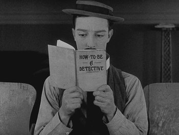 Movie still from “Sherlock Jr.” (1924), directed by Buster Keaton – A man in a hat is holding a book; Medium shot, High angle