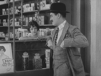 Movie still from “Sherlock Jr.” (1924), directed by Buster Keaton – An old photo of a man and a woman in a store; Medium shot, Over the shoulder angle