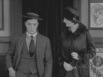 Movie still from “Sherlock Jr.” (1924), directed by Buster Keaton – A man and a woman standing next to each other in front of a building; Medium shot, High angle