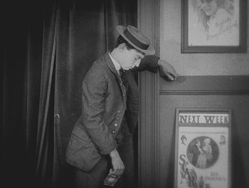 Movie still from “Sherlock Jr.” (1924), directed by Buster Keaton – A man in a suit and hat holding a cell phone in his hand; Medium shot, High angle