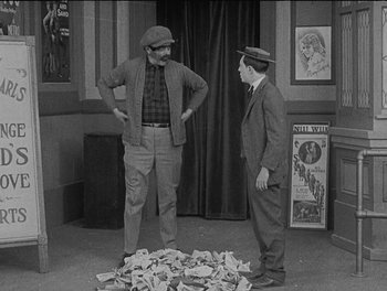 Movie still from “Sherlock Jr.” (1924), directed by Buster Keaton – A couple of men standing next to a pile of money; Wide shot, High angle