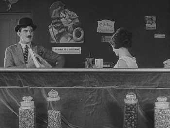 Movie still from “Sherlock Jr.” (1924), directed by Buster Keaton – A man and a woman sitting at a counter; Wide shot, High angle