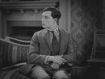 Movie still from “Sherlock Jr.” (1924), directed by Buster Keaton – A man sitting on a couch in a suit and tie; Medium shot, High angle