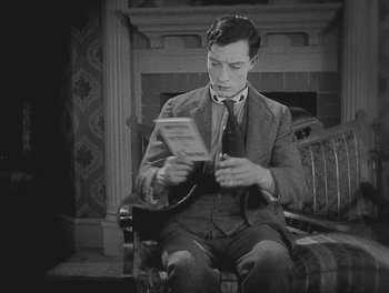 Movie still from “Sherlock Jr.” (1924), directed by Buster Keaton – A man sitting in a chair looking at a newspaper; Medium shot, High angle