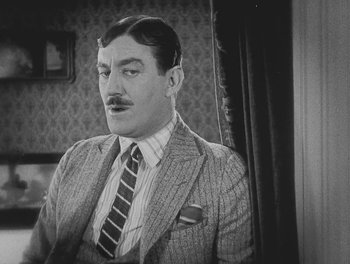 Movie still from “Sherlock Jr.” (1924), directed by Buster Keaton – A man in a suit and tie sitting in front of a curtain; Close Up shot, Low angle
