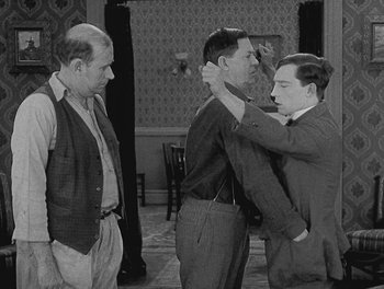 Movie still from “Sherlock Jr.” (1924), directed by Buster Keaton – A man is putting a tie on another man's neck; Medium shot, Over the shoulder angle