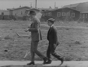 Movie still from “Sherlock Jr.” (1924), directed by Buster Keaton – A man and a boy walking down a sidewalk; Wide shot, Low angle